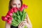 Woman with a bouquet of red tulips on a yellow background. Happy girl in a black dress holds an armful of flowers . Gift