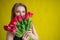 Woman with a bouquet of red tulips on a yellow background. Happy girl in a black dress holds an armful of flowers . Gift