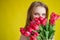 Woman with a bouquet of red tulips on a yellow background. Happy girl in a black dress holds an armful of flowers . Gift