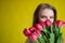 Woman with a bouquet of red tulips on a yellow background. Happy girl in a black dress holds an armful of flowers . Gift