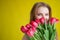 Woman with a bouquet of red tulips on a yellow background. Happy girl in a black dress holds an armful of flowers . Gift