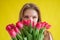 Woman with a bouquet of red tulips on a yellow background. Happy girl in a black dress holds an armful of flowers . Gift