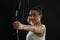 Woman with bow and arrow practicing archery against black background, focus on hand