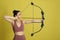 Woman with bow and arrow practicing archery on yellow background