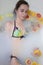 Woman in bright swimsuit in milk bath with oranges, lemons, grapefruits and book pages. Spa and skin care concept.