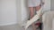 A woman with a broken leg in plaster moves around the room on crutches at home