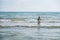 Woman bruenette with long hair in blue bikini walking in the sea water with waves. Side view.