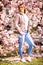 Woman with brunette short hair with streaks in jeans and quilted vest in portrait between blooming cherry trees.