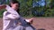 Woman brushes off midges sitting in forest by lake reading smartphone.