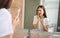 Woman brushing teeth with sensitive teeth and hands touch the cheeks and looking in the mirror, towel on the shoulder on bathroom.