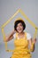 Woman builder wearing yellow protect helmet and overall holding house frame