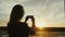 A woman in a business suit takes a photograph of a sunset in a window. In an office building or airport terminal