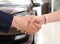 Woman buying car and shaking hands with salesman against blurred auto