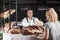 Woman buying fresh bread from cheerful baker in shop