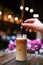 a woman in a cafe drinks a cold cappuccino. hand holds a straw in a glass with coffee. summer cool drinks