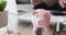 Woman calculating finances putting coin into piggy bank box, closeup