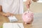 Woman with calculator and organizer book connecting piggy bank with electric plug.