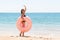 Woman calls to swim in the sea and waves her hand. Girl relaxing with donut on the beach and playing with inflatable ring. Summer