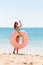 Woman calls to swim in the sea and waves her hand. Girl relaxing with donut on the beach and playing with inflatable ring. Summer