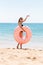 Woman calls to swim in the sea and waves her hand. Girl relaxing on inflatable ring at the beach. Summer holidays and vacation