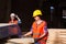 Woman carpenter working at wooden factory. Workers in protective helmet, vest and gloves at factory.