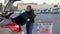 Woman carries a modern large TV in a supermarket trolley and tries to load it into the trunk of a car on the parking