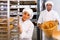 Woman carrying baked baguettes on trolley rack working in bakery