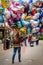 Woman carrying many floating gas balloons with different cartoon characters outdoors.