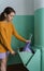 A woman in casual clothes throws a bag of garbage into the garbage chute. Vertical foto