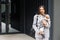 Woman in casual jacket hugging her favorite fluffy trained purebred Jack Russell Terrier dog dressed in suit for dogs near wall in