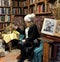 Woman and cat sitting in front of shelves full of old books. Shakespeare & Company, Paris, France.