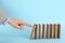 Woman causing chain reaction by pushing domino tile on light blue background, closeup