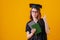 Woman celebrating her graduation, wearing gown and hat. Over orange background