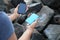 Woman charging smartphone with power bank on rocky mountain, closeup