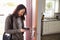 Woman Checking Mobile Phone As She Opens Door Of Apartment