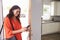 Woman Checking Mobile Phone As She Opens Door Of Apartment