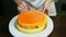 Woman in chef uniform decorating orange glazed cheesecake by mini macaroons