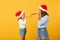 Woman child baby girl in Christmas Santa hat blow in pipe. Mommy little kid daughter isolated on yellow background