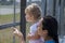 A woman and a child look into the distance through a fence with a small net, the mother points at something to the child.