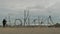 A woman and child visit Hokitika sign made from driftwood on the beach at Hokitika