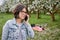 A woman with children looks at a grazing cow on the background of a blooming garden and green grass. Blanket with laptop and