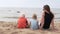 Woman with children sits on the beach and looks at the sea