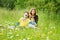 A woman with children is sitting in the high green grass in the mountains and dine. They laugh and have fun together