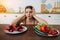 Woman is choosing between fruits and sweets while standing on light kitchen.