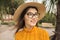 Woman in the city is having fun, laughing. Palm trees in the background. Bright yellow clothes, glasses, hat.