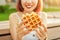 Woman in a city Park is having lunch and holding a Viennese waffle sandwich. Modern delicious and high calorie street food