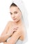 Woman with clean face and towel on her head applying moisturizer cream on shoulders. .