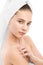 Woman with clean face and towel on her head applying moisturizer cream at shoulders. Isolated.