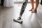 Woman cleaning a floor with cordless vacuum cleaner in the room with modern design interior. Easy removing of dirt.