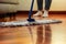 A woman cleaning the hardwood floor, with a close-up of the mop and a blurred background of feet and a sofa.